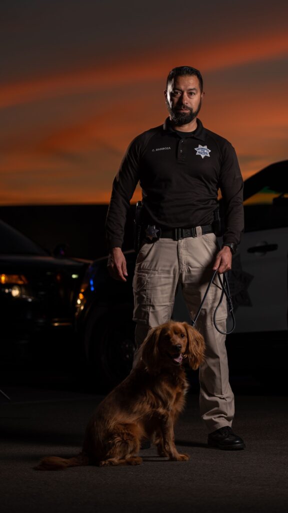 Salinas police officer standing with his dog in front of a backdrop